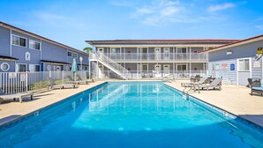 A swimming pool with a white fence, lounge chairs, and a building with balconies. - Walk to the Beach | 2 Pools | Military Welcome! (Biloxi)