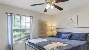 Une chambre à coucher avec un lit, un ventilateur de plafond, une fenêtre avec des rideaux et une lampe fixée au mur.
