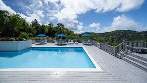 Piscina com espreguiçadeiras e guarda-sóis, cercada por um deck de madeira e vegetação.