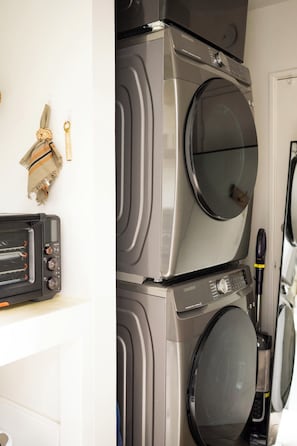 A stacked washer and dryer unit with a microwave and a small appliance on the counter.