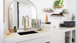 A modern kitchen with a large sink, a double faucet, and a built-in oven. There are shelves above the sink holding various kitchen items.
