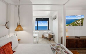 A bedroom with a bed, a hanging lamp, a TV, and a view of the sea.