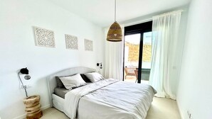Een slaapkamer met een bed, een bedlampje, een decoratief wandobject en een raam met gordijnen.