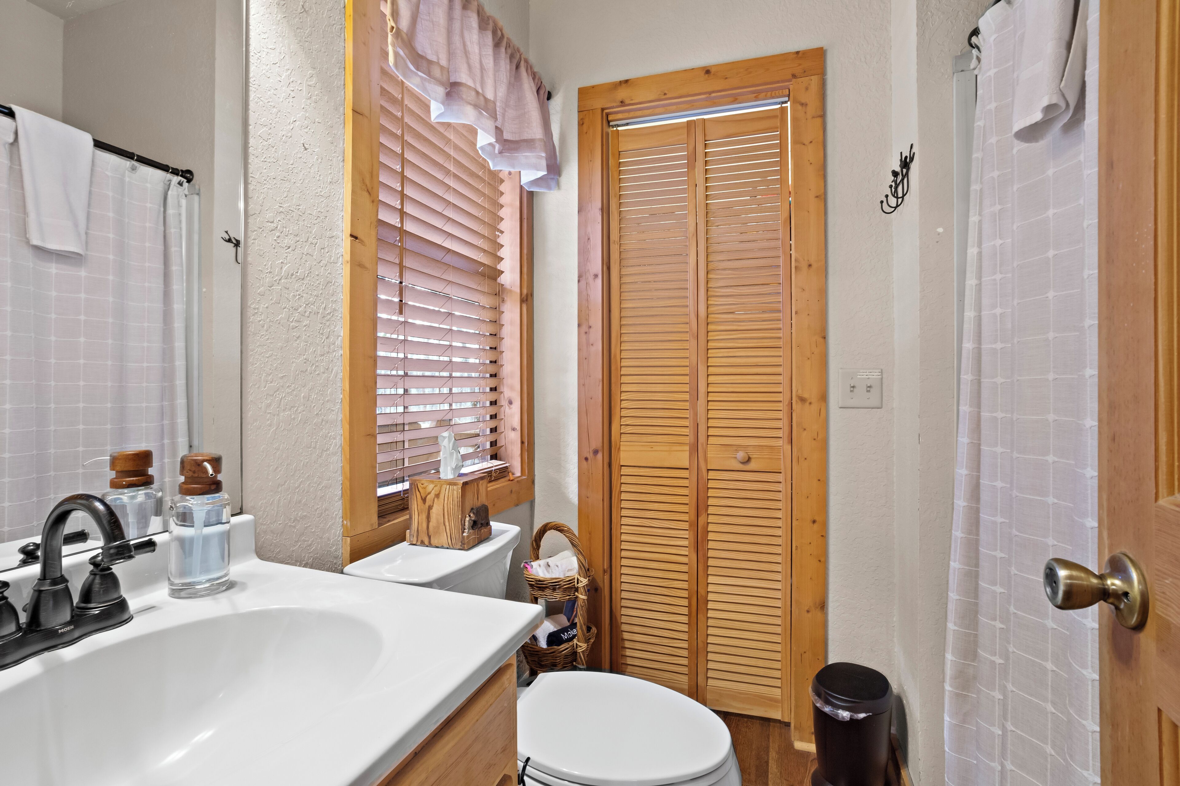 A bathroom with a sink, mirror, toilet, and wooden door.