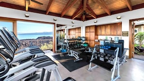 A gym with treadmills, dumbbells, and exercise balls, featuring wooden beams and large windows overlooking a scenic view. - Halii Kai Resort by KBM (Waikoloa)