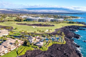 A resort with multiple buildings, a golf course, and a coastline. - Halii Kai Resort by KBM (Waikoloa)