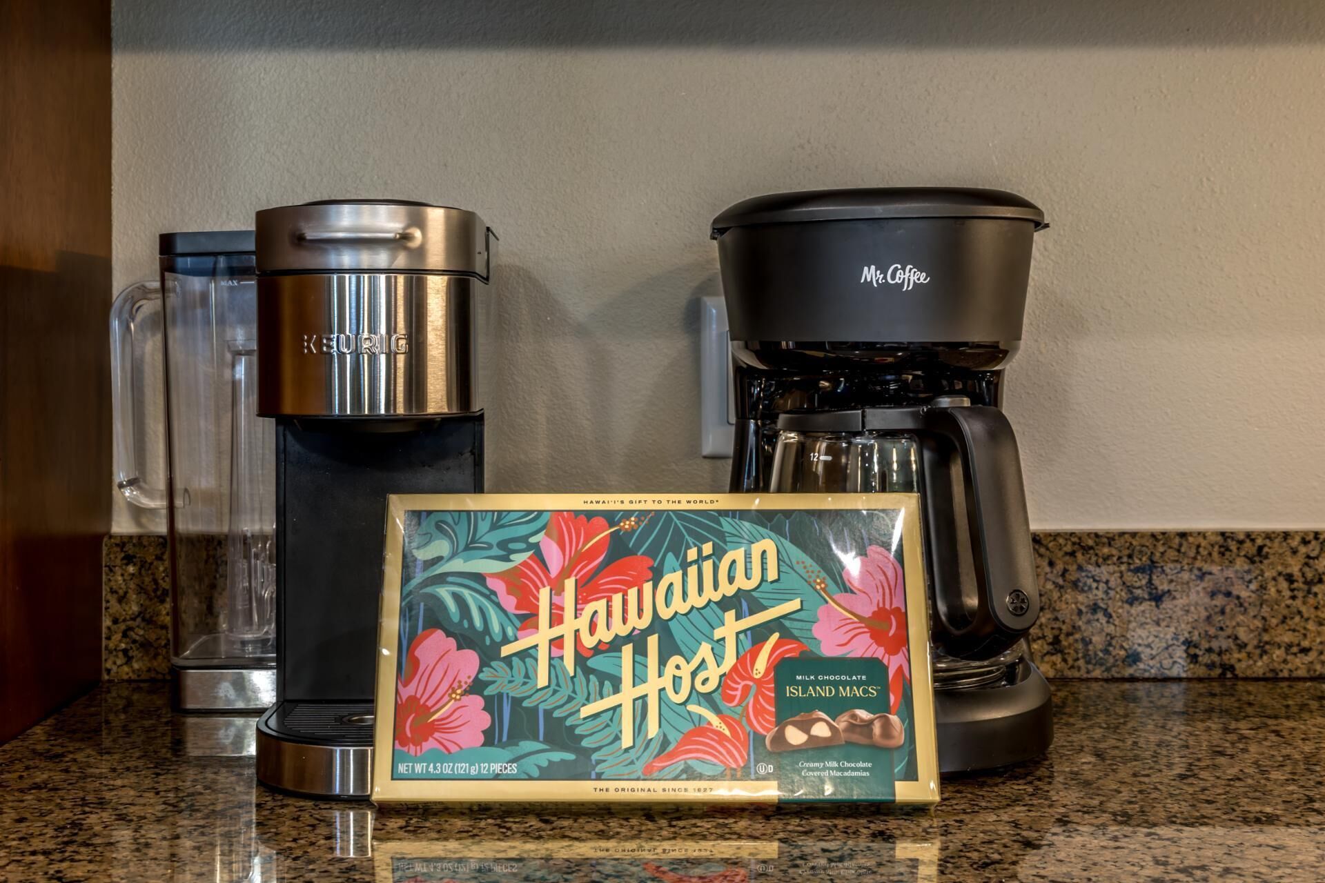En kaffebryggare, en Keurig-kaffebryggare och en ask med Hawaiian Host-mjölkchoklad med macadamianötter från Hawaii står på en köksbänk.