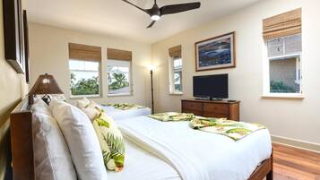 A bedroom with two beds, a ceiling fan, a TV, and windows with views of palm trees.