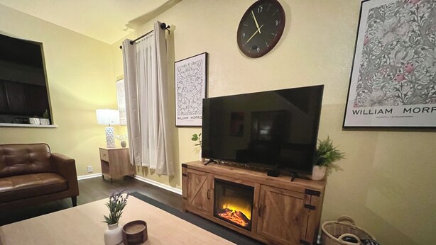 A living room with a television, fireplace, sofa, and a clock on the wall. - Charming 3-bedroom townhome, BMT Lackland, near SeaWorld, & 15mins to Downtown (San Antonio)