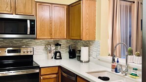 A kitchen with wooden cabinets, a microwave, stove, and a sink with a faucet. - Charming 3-bedroom townhome, BMT Lackland, near SeaWorld, & 15mins to Downtown (San Antonio)