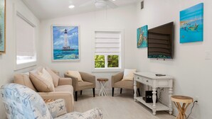 Un salon avec un canapé beige, deux fauteuils, une petite table ronde, une console blanche et des œuvres d’art accrochées aux murs.