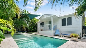 Une piscine avec une maison blanche en arrière-plan, le tout entouré d’une végétation luxuriante.