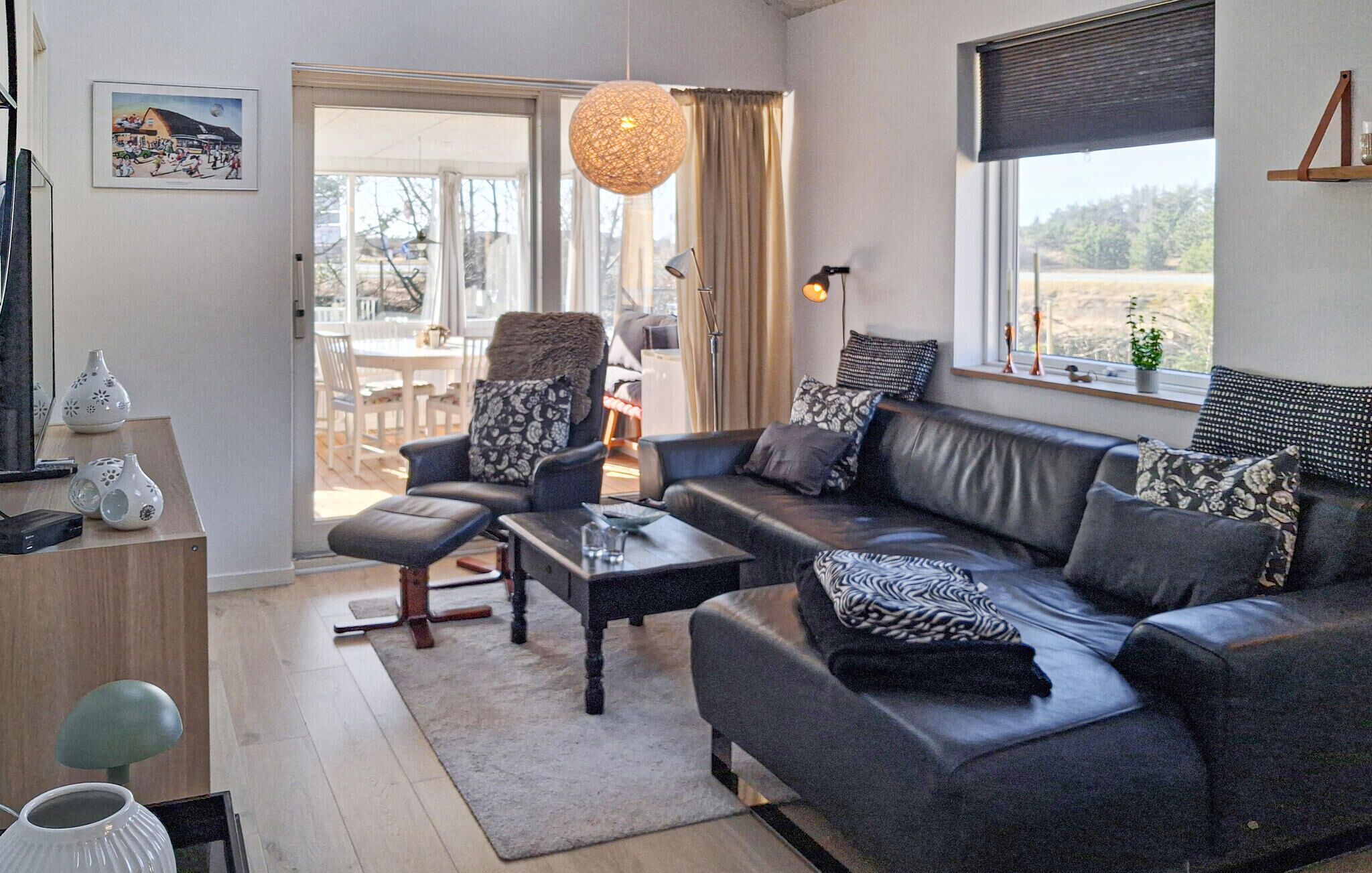 Un salon moderne comprenant un canapé, un fauteuil, une table basse et un coin repas visible à travers une porte vitrée.