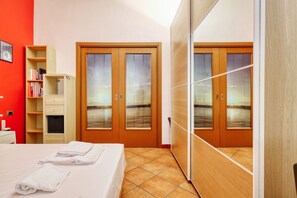 A hotel room with a bed, two wardrobes, a bookshelf, and a view of the sea through the wardrobe doors.
