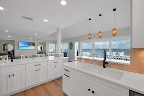 A modern kitchen with white cabinetry, a large island, and a view of the ocean. - Ocean Sunrise – Bayfront Luxury with Pool, Dock & Game Room. Steps to Gulf. Perfect for Families. (Bradenton Beach)