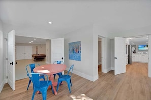 A spacious room with a round table and chairs, a painting on the wall, and a visible kitchen area. - Ocean Sunrise – Bayfront Luxury with Pool, Dock & Game Room. Steps to Gulf. Perfect for Families. (Bradenton Beach)