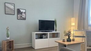 A modern living room with a flat-screen TV on a white cabinet, a grey sofa, and a wooden coffee table. There are two framed pictures on the wall and a small plant on the cabinet. - Strandnixe - A little time out - A little time out for relaxing days... Beach - and (Dahme)