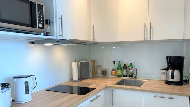 A modern kitchen with white cabinets, a microwave, a kettle, a coffee maker, and various bottles on the counter. - Strandnixe - A little time out - A little time out for relaxing days... Beach - and (Dahme)