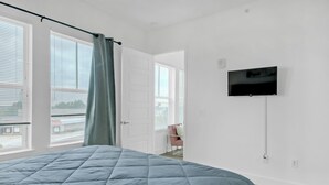 Ein Schlafzimmer mit einem Bett, einem an der Wand montierten Fernseher und einem Fenster mit Vorhängen.