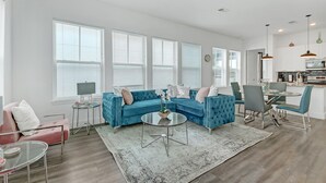 Ein modernes Wohnzimmer mit einem blauen Ecksofa, einem Glastisch und einem Essbereich mit rundem Tisch und Stühlen.