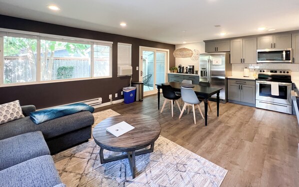 A modern kitchen with stainless steel appliances, a dining area with a table and chairs, and a living room with a sofa and a coffee table. - Charming 2-bedroom at Issaquah Front St (Issaquah)
