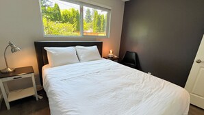A neatly made bed with white linens, a bedside lamp, and a window with a view of greenery. - Charming 2-bedroom at Issaquah Front St (Issaquah)