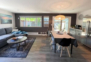 A modern living room with a grey sofa, a round coffee table, and a dining area with a long table and chairs. - Charming 2-bedroom at Issaquah Front St (Issaquah)