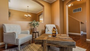 Un salon avec une table basse en bois, deux fauteuils, une petite table d’appoint avec une plante, et un escalier en arrière-plan.