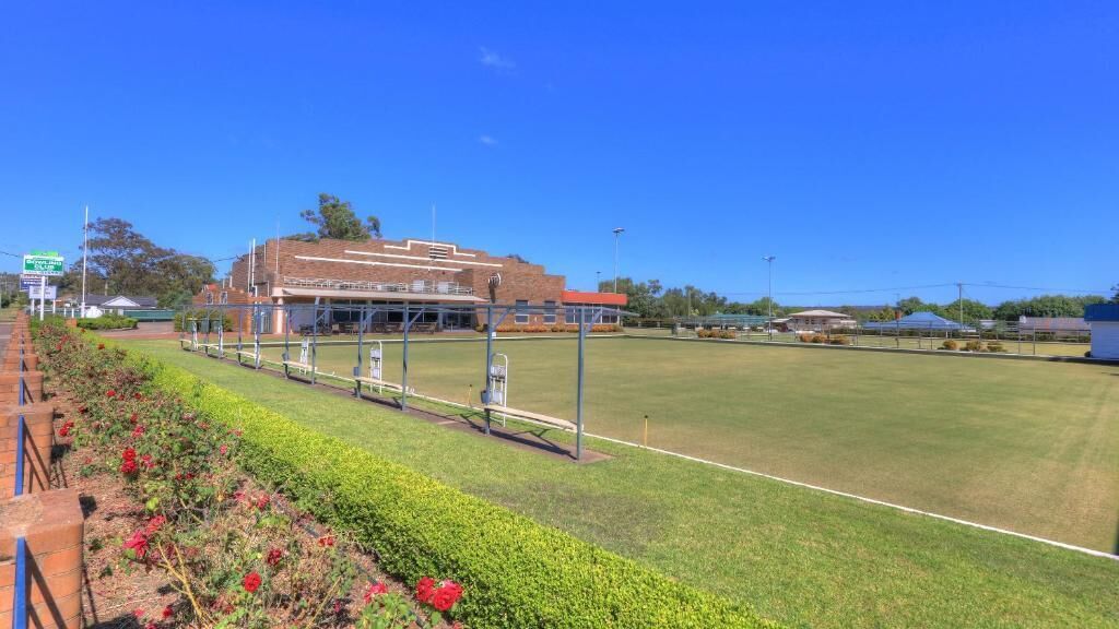 A sports field with a building in the background, a fence, and a clear sky.