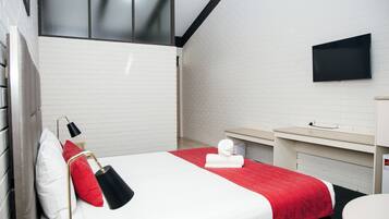Una habitación de hotel con cama, televisor montado en la pared, una mesita y una ventana.