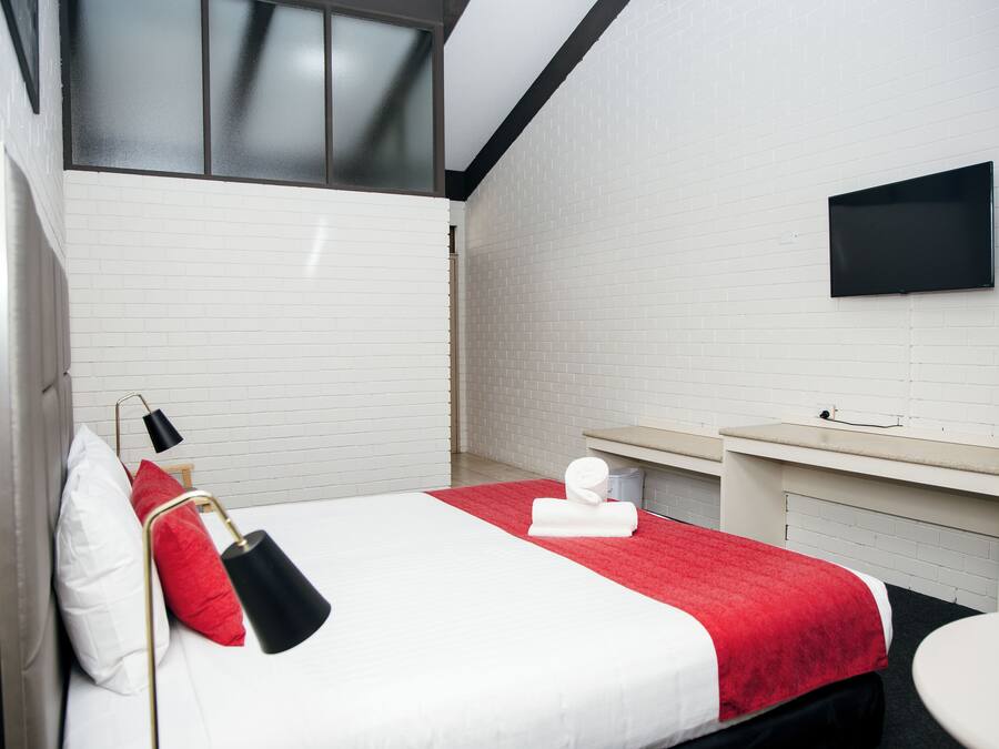 Una habitación de hotel con cama, televisor montado en la pared, una mesita y una ventana.