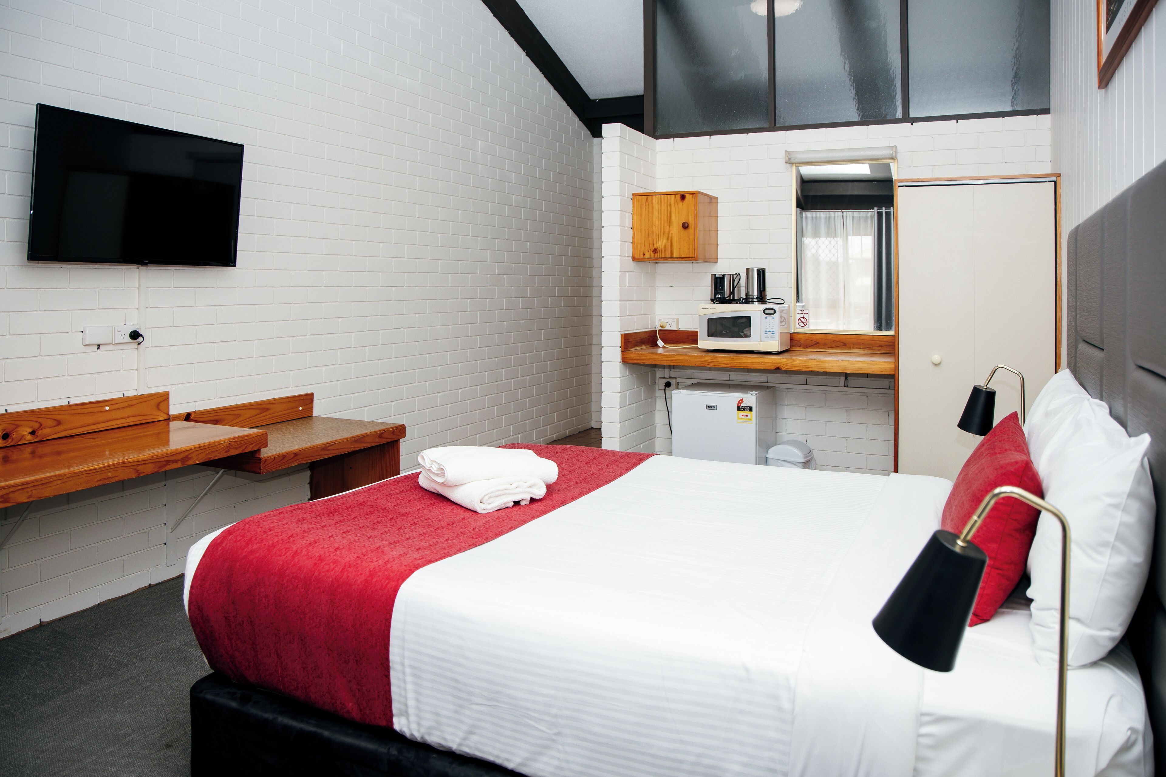Une chambre d’hôtel équipée d’un lit, d’un téléviseur fixé au mur, d’un four à micro-ondes et d’un petit placard.