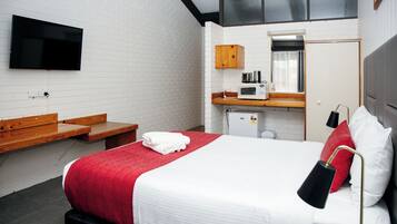 Une chambre d’hôtel équipée d’un lit, d’un téléviseur fixé au mur, d’un four à micro-ondes et d’un petit placard.