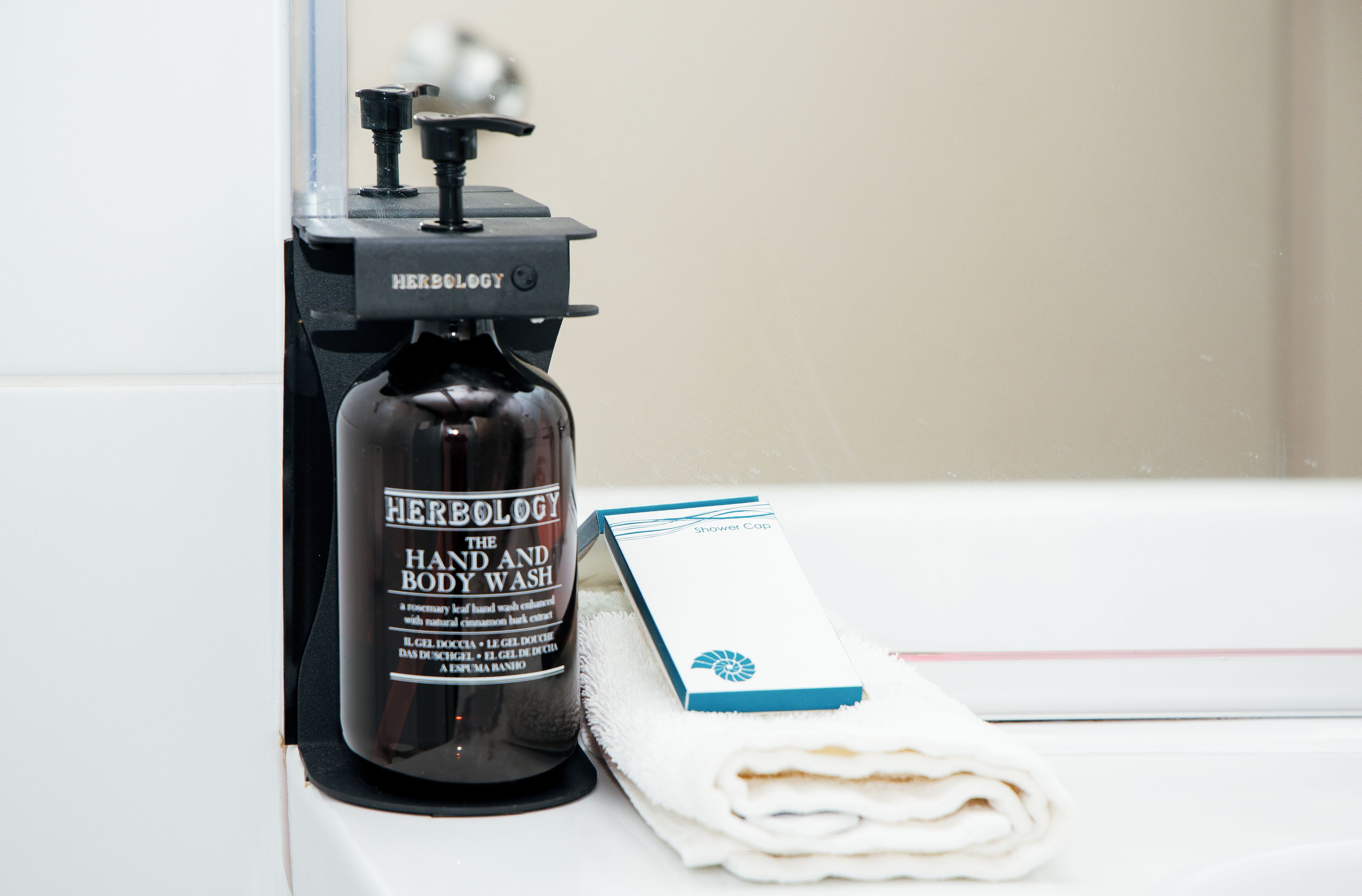 Casa de banho com frasco preto de gel de banho e corpo, toalha branca e touca de banho.