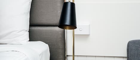 Una cama bien hecha con ropa blanca, una mesita de noche con lámpara y otra mesita de noche con control remoto.
