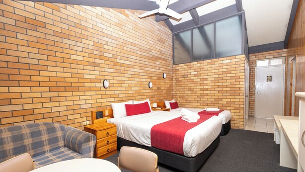 Une chambre d’hôtel avec un mur en briques, un lit double avec une literie rouge, un canapé, un bureau et une chaise.