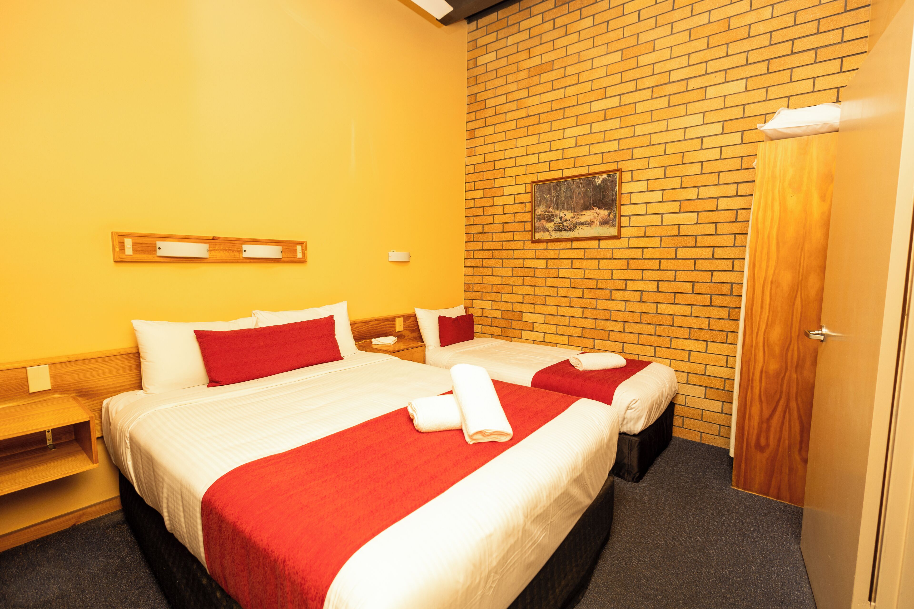 A hotel room with two beds, a brick wall, and a wooden door.