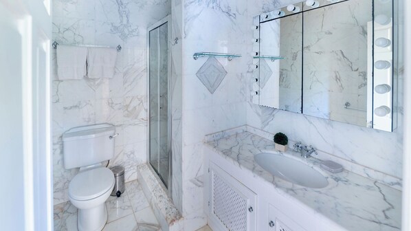 A bathroom with a toilet, shower, and sink, all with marble flooring and walls.