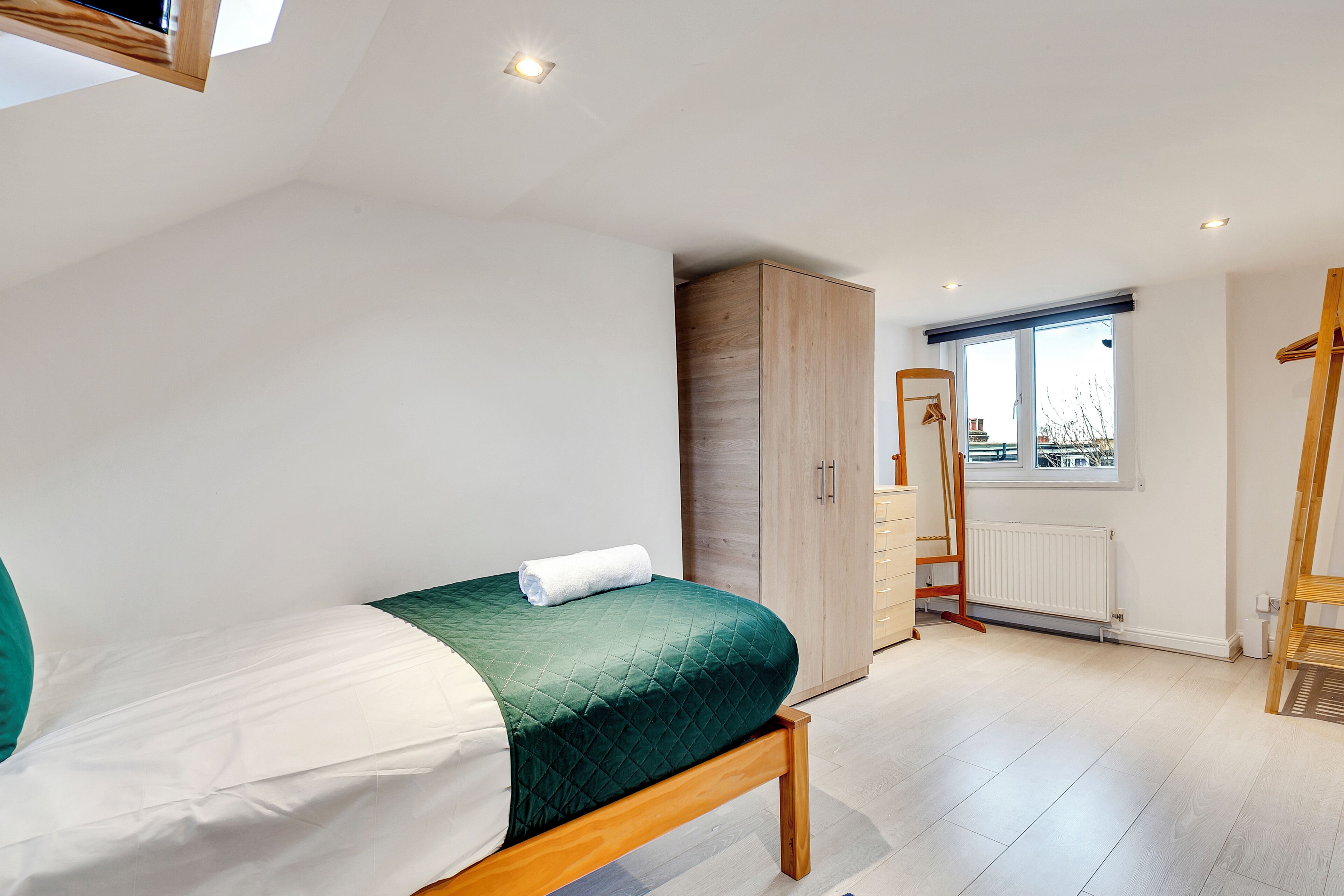 A bedroom with a bed, a wardrobe, a radiator, and a window.