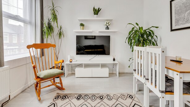 Un salon avec un téléviseur, des meubles blancs et des plantes.