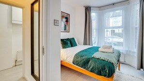 Une chambre à coucher avec un lit, une fenêtre avec des rideaux, un radiateur et un tableau accroché au mur.