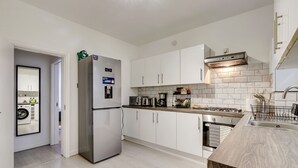Une cuisine moderne avec des armoires blanches, un réfrigérateur en acier inoxydable, un four encastré et un plan de travail en bois.