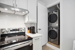 A compact kitchen with a built-in oven, a coffee maker, and a washer-dryer unit. - Private 1BR Suite, New Build, 2 Guests, No Smoking (North Vancouver)