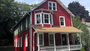 Une maison rouge à deux étages, dotée d’un porche à l’avant, de boiseries blanches et d’un petit jardin fleuri.