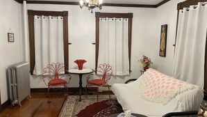 Une pièce chaleureuse avec un plancher en bois, une table ronde entourée de chaises, un canapé avec un plaid, un radiateur et un lustre.