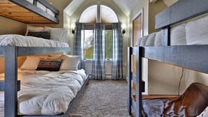 A bunk bed room with a high ceiling and a large window with curtains.