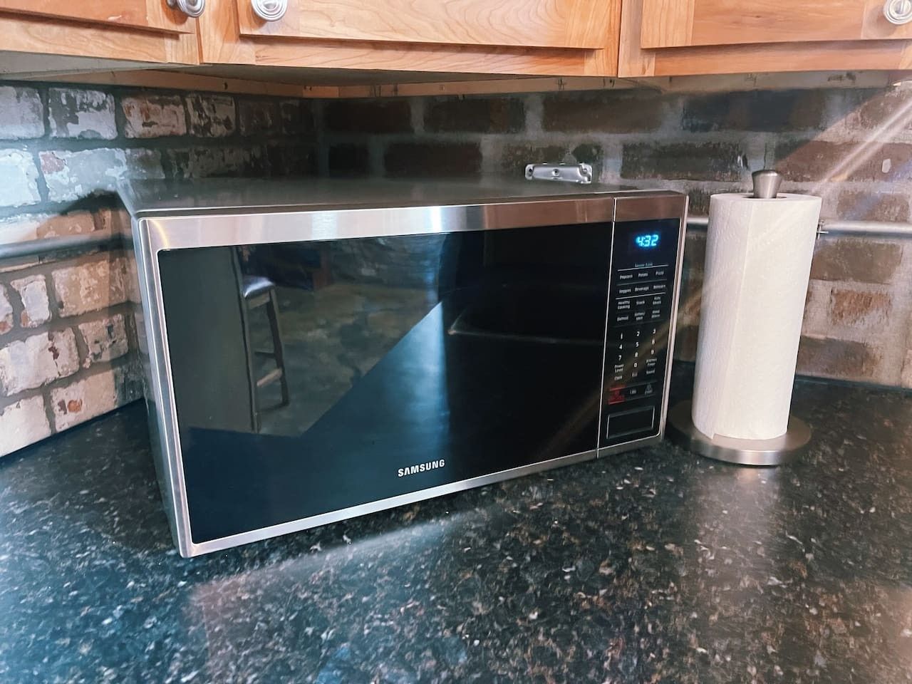 Een rvs magnetron met een digitaal scherm, geplaatst op een granieten aanrecht.