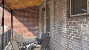 A covered patio with a brick wall, a table with chairs, and a window. - The Nest at Main Street Suites: Unique Apt in historic downtown Van Buren, AR (Van Buren)