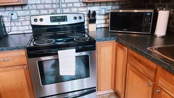 A kitchen with a stainless steel stove, a microwave, wooden cabinets, and a brick wall.