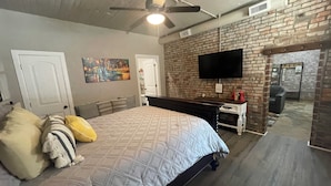 A bedroom with a bed, a desk, a TV, and a brick wall. - The Nest at Main Street Suites: Unique Apt in historic downtown Van Buren, AR (Van Buren)